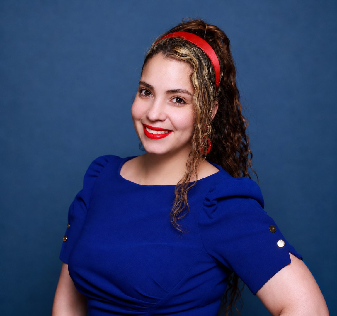 Nayeli Castillo in a confident three-quarter pose, smiling at the camera, cobalt blue dress and red headband against a deep indigo studio background.