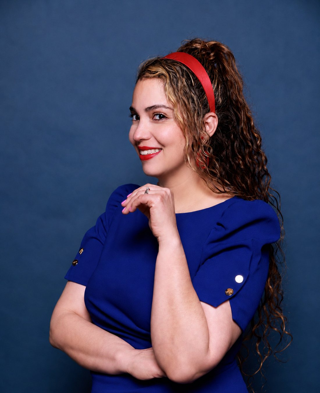 Nayeli Castillo in joyful side profile, laughing, in a cobalt blue dress against a deep indigo studio background.